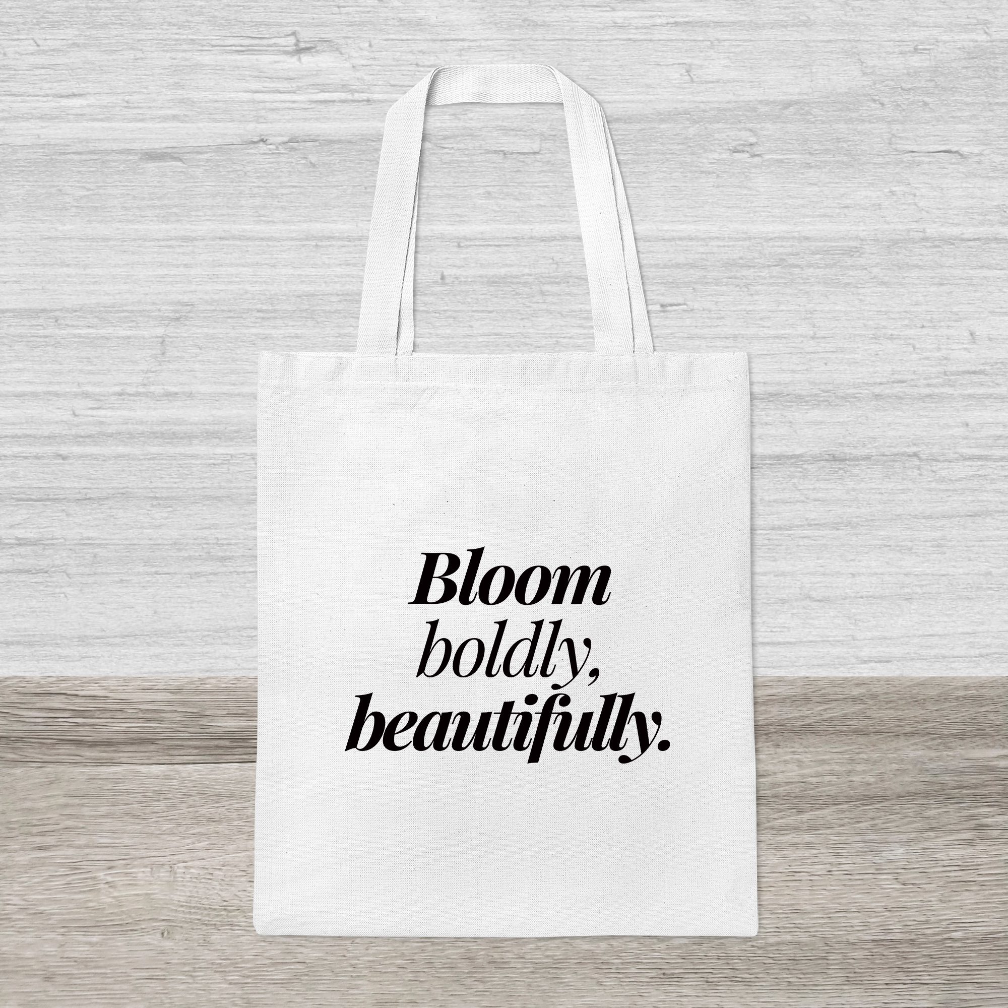 Canvas Tote Bag – Bloom Boldly Beautifully Minimalist Design White canvas tote bag with “Bloom boldly, beautifully” printed in bold black serif font