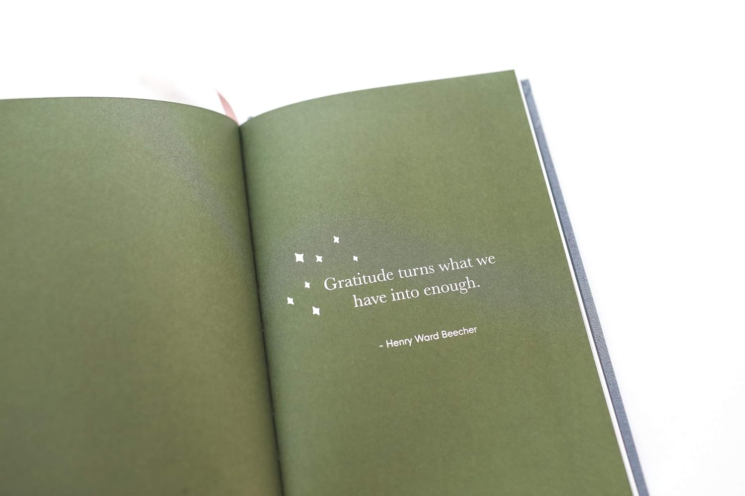 Gratitude Quote – Henry Ward Beecher Open book with a green page displaying the quote “Gratitude turns what we have into enough” by Henry Ward Beecher, surrounded by white star-like symbols.