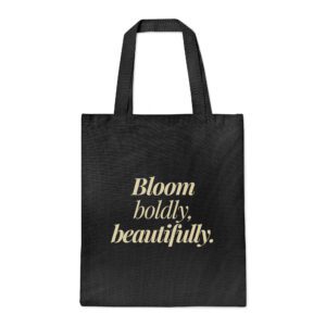 Black canvas tote bag with “Bloom boldly, beautifully” in beige italic serif font