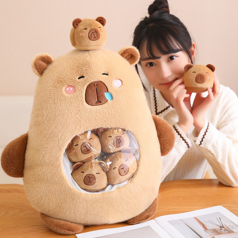 Capybara Plush Toy – Bear Belly Hug Edition A young woman sitting beside a large capybara plush toy with a transparent belly pocket filled with smaller bear plushies. She is smiling and holding one of the mini plush bears.