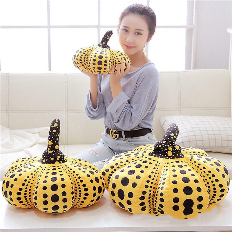 Pumpkin Plushies – Trio of Playful Comfort Person holding a yellow pumpkin plushie with two larger versions on a white table