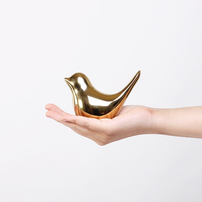 Golden Bird Soft Decoration – Handheld Glow Edition Hand holding a gold bird-shaped sculpture with rounded body and pointed tail.