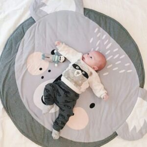 Baby lying on a koala-themed crawling mat with gray ears and a friendly face.