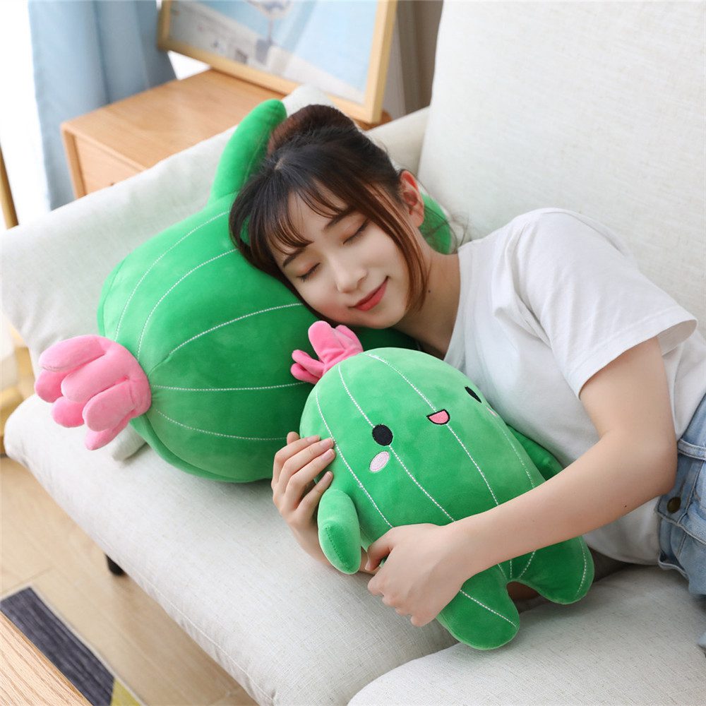 Cactus Plush Toy – Snuggle Bloom Pair Person lying on couch cuddling two cactus plush toys, one large and one small, both with pink flowers.