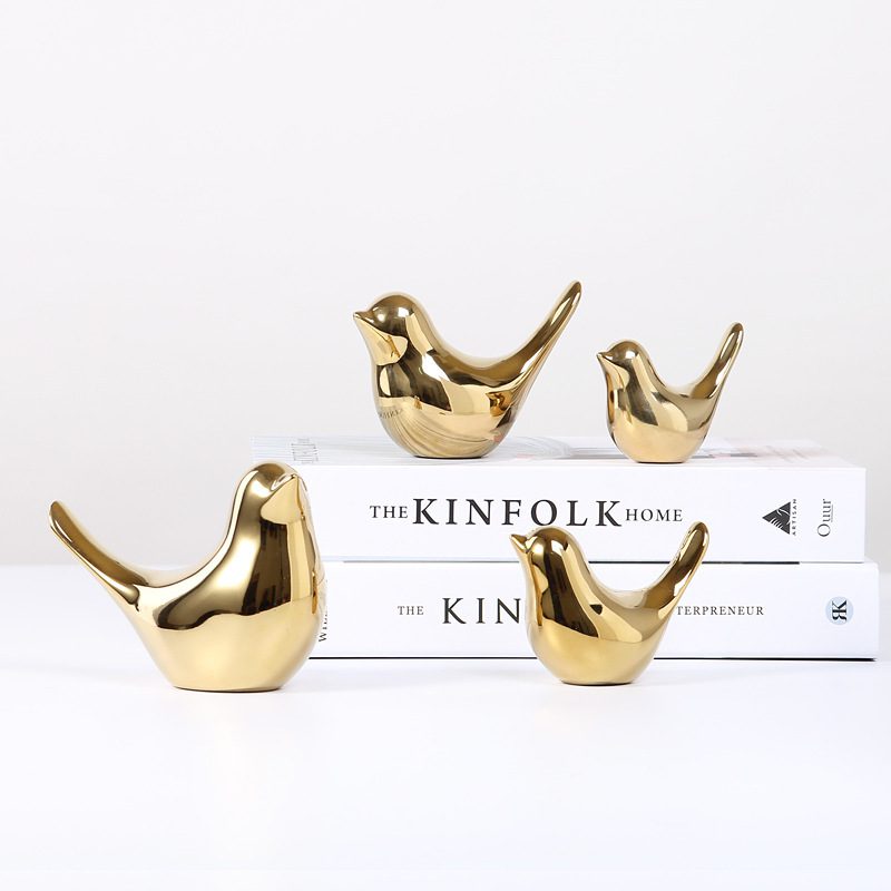 Golden Bird Soft Decoration – Quartet Display Edition Four gold bird figurines placed on stacked books titled “THE KINFOLK HOME” and “THE KINFOLK ENTREPRENEUR.”