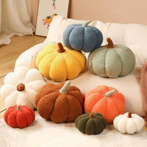A cozy collection of plush pumpkin pillow ornaments in various colors and textures, arranged on sofas, blankets, and wooden floors. Each pillow mimics the segmented shape of a real pumpkin with soft stems and fuzzy fabric.