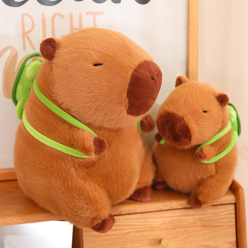 Capybara Plush Toy – Duo Explorer Edition Two capybara plush toys with green backpacks sitting on a wooden surface.