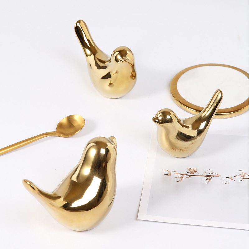Golden Bird Soft Decoration – Trio Nest Edition Three gold bird figurines arranged with a spoon, coaster, and floral card on a white surface.