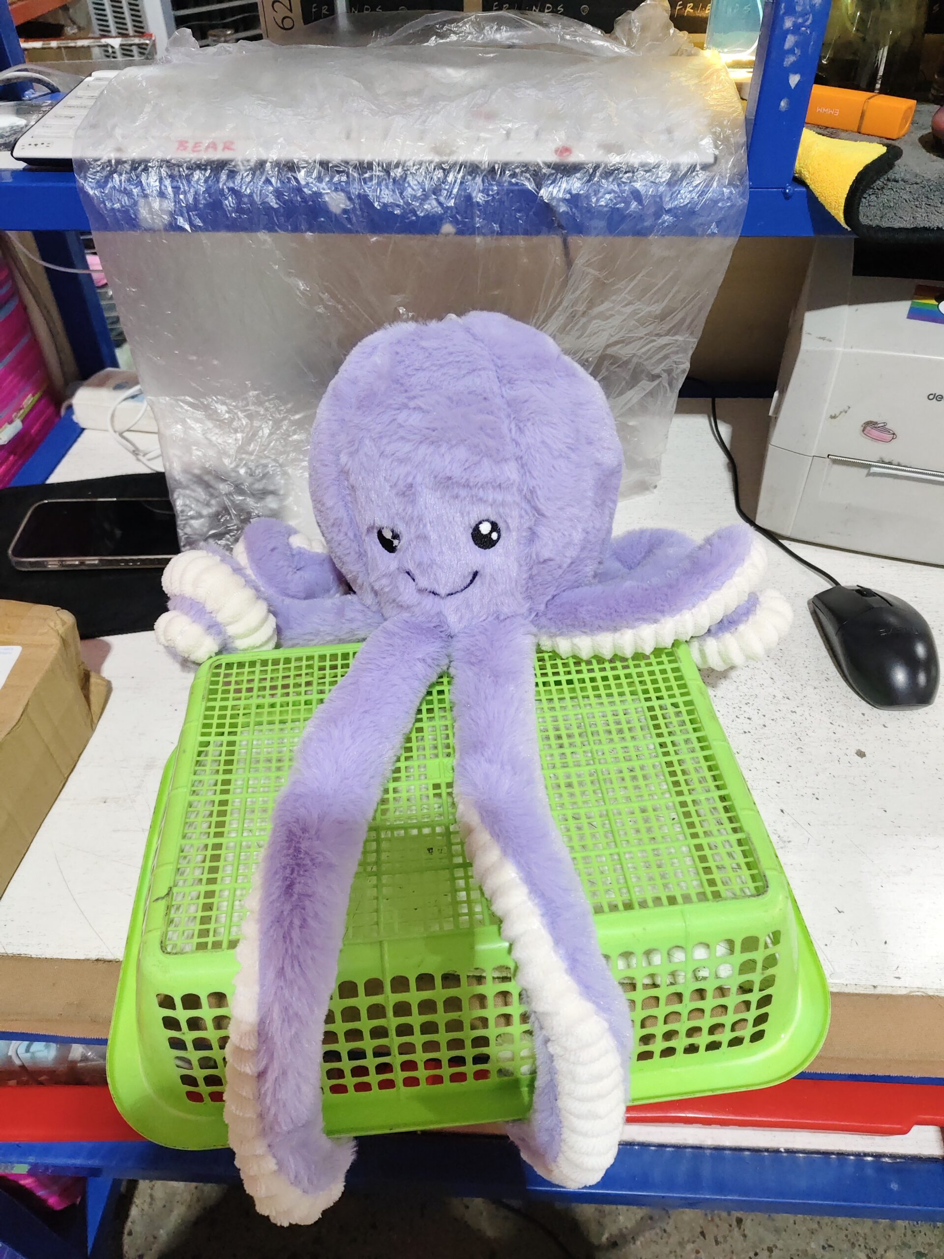 Octopus Stuffed Animal Plushie – Soft Workspace Accent Light purple octopus stuffed animal plushie on a green basket in a room with office supplies and shelving.