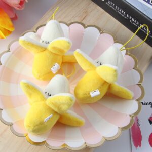 Four peeled banana keychain plush toys with smiling faces arranged on a scalloped plate with pink and white segments.