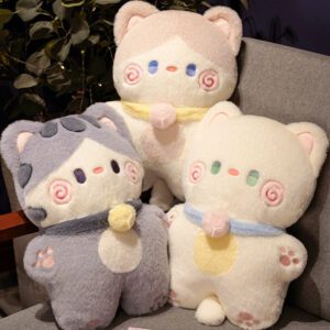 Three Hug Cats Plush Toys in gray, cream, and beige seated on a chair with spiral cheeks and colorful collars.