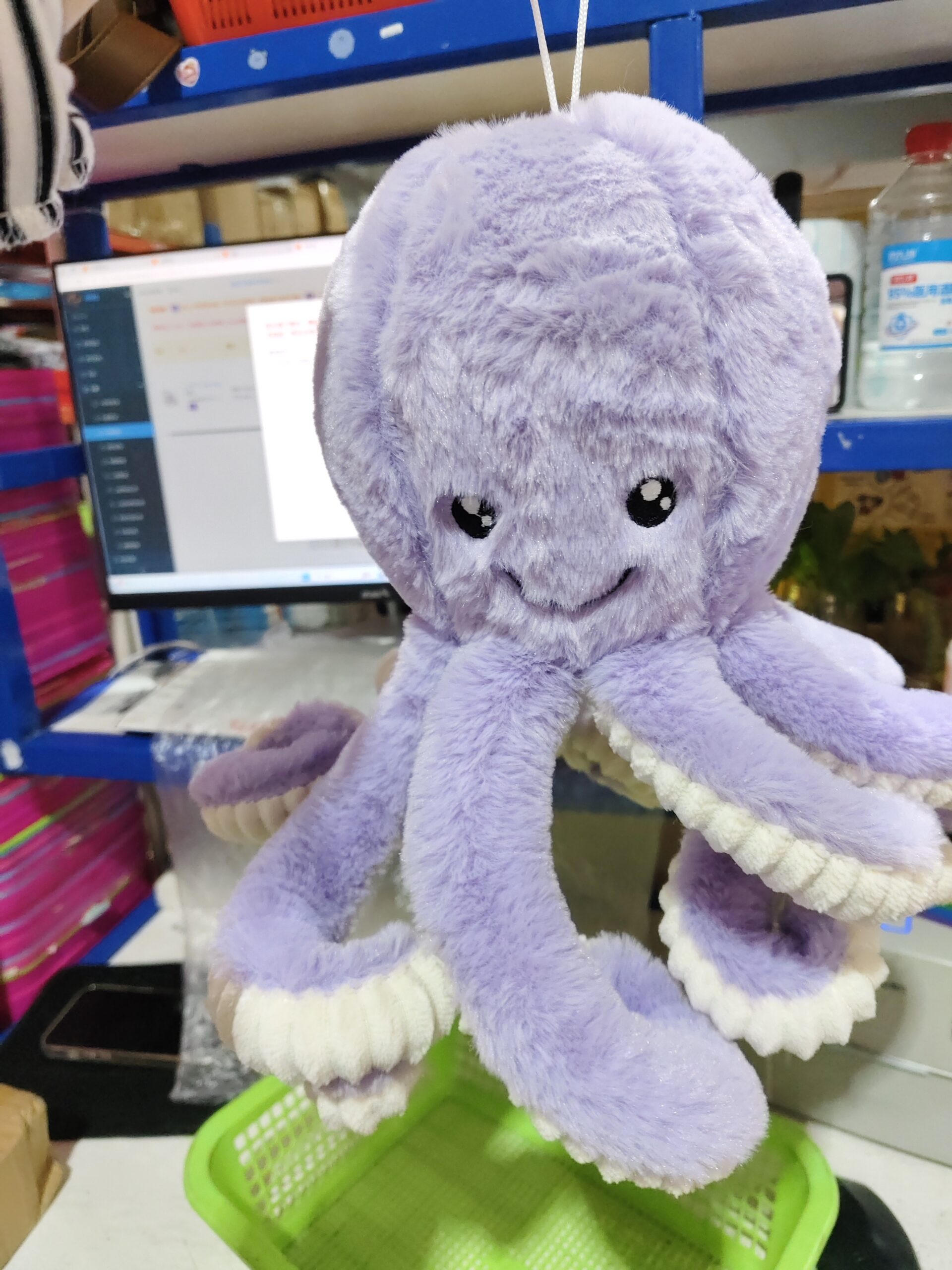Octopus Stuffed Animal Plushie – Playful Lift Edition Light purple octopus stuffed animal plushie held by a string above a green plastic basket.