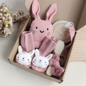 Pink bunny-themed newborn gift box set with socks, teether, pacifier clip, headband, and hairbrush.