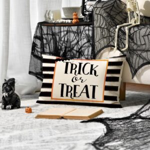 Halloween-themed indoor setup featuring a striped pillow with “TRICK or TREAT” text, skeleton figure, spiderweb fabric, and pumpkins.