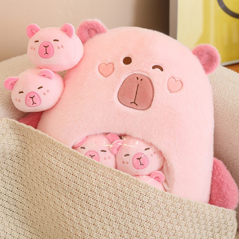 Capybara Plush Toy – Love Nest Edition Pink capybara plush toy with heart-shaped eyes and smaller bear heads tucked under a blanket.